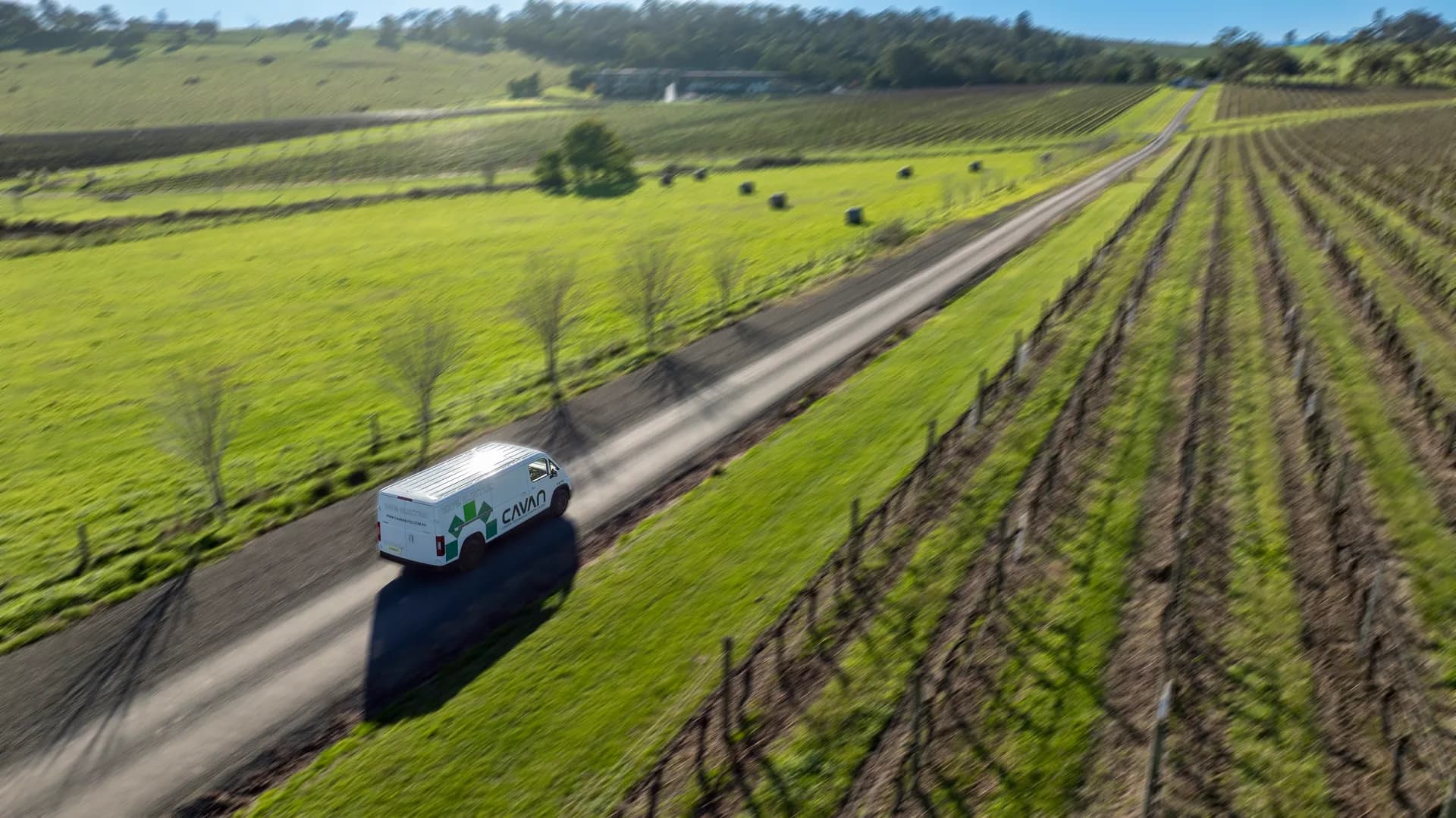Aerial view of a Cavan electric van on a tree-lined country road between paddocks and vines