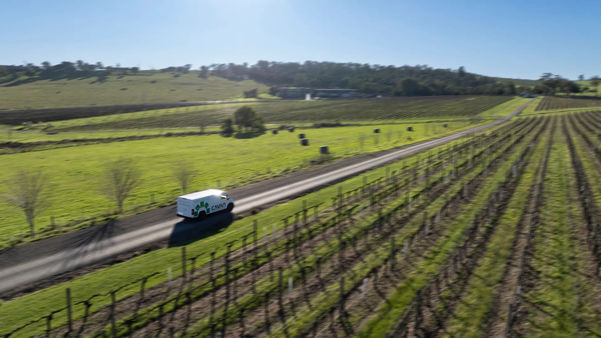 Aerial view of a Cavan electric van on a straight country road between vineyards and hay bales