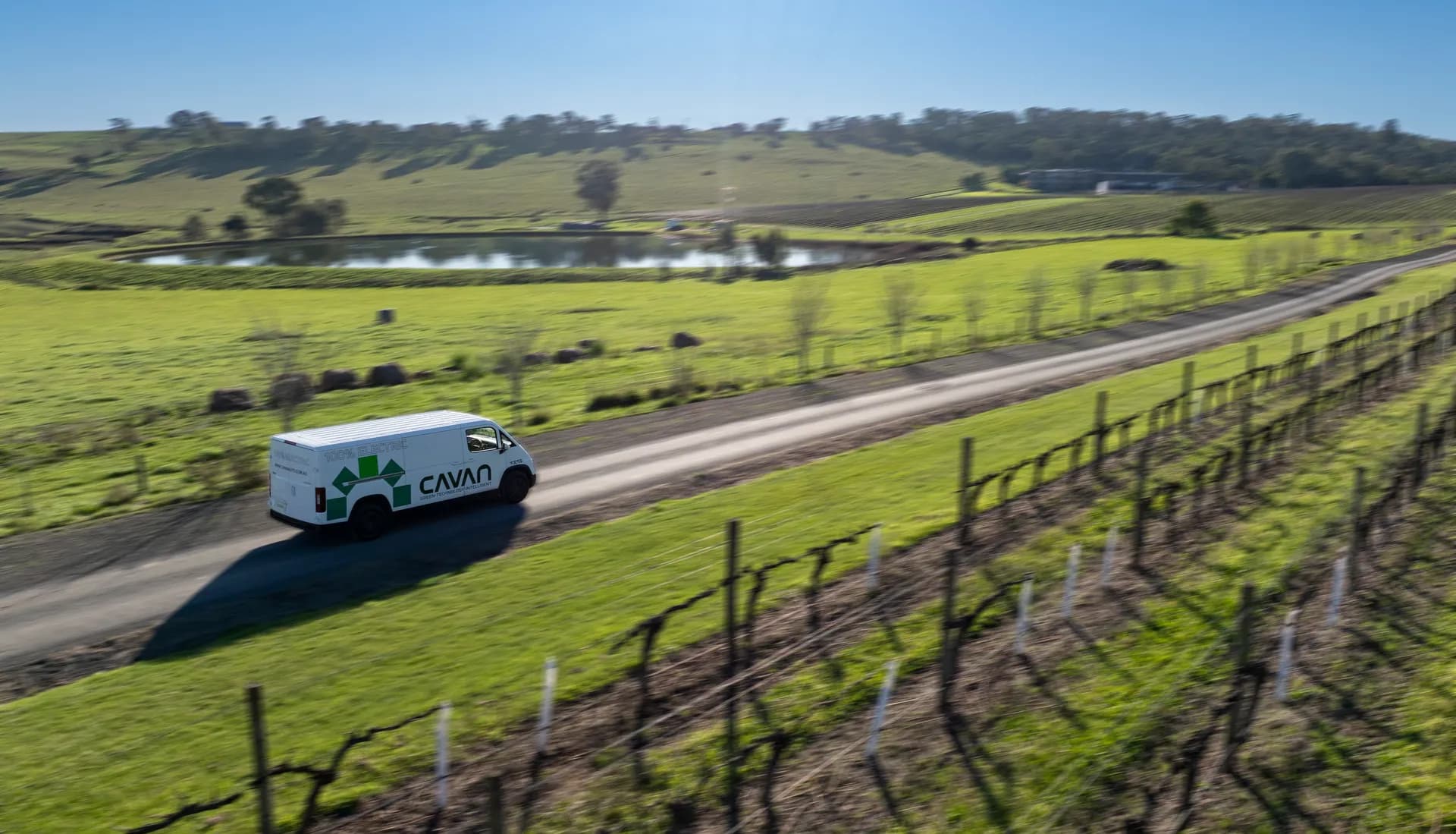 Aerial view of a Cavan electric van heading past a dam toward a hillside winery