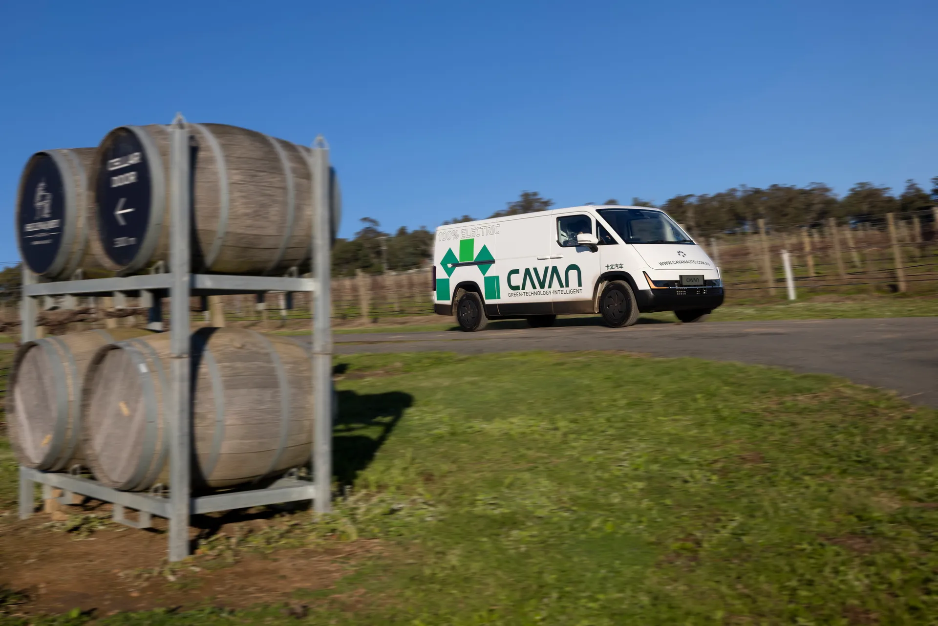 A Cavan electric van passing a winery cellar door, framed by stacked wine barrels