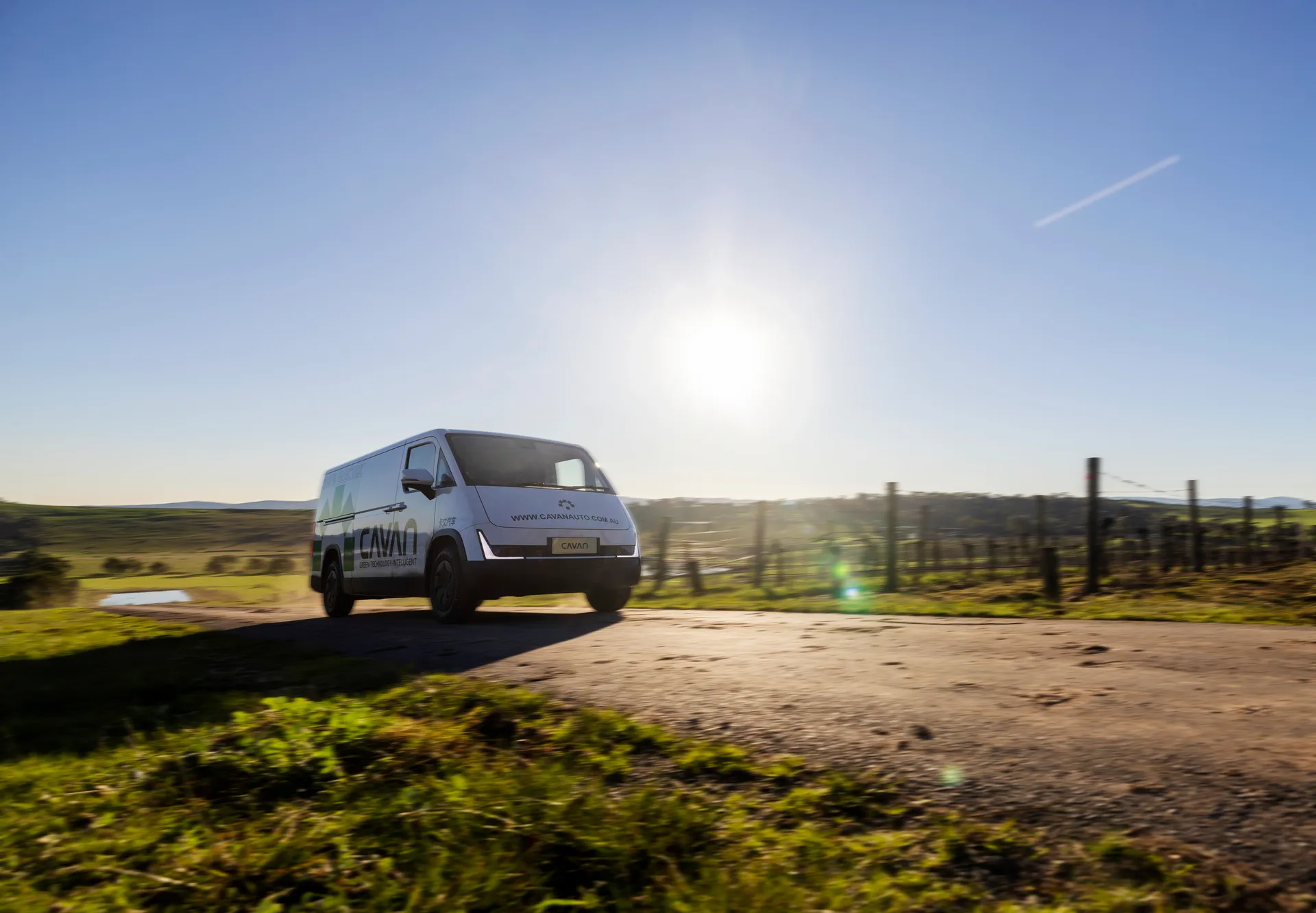 A Cavan electric van driving into low morning sun beside a vineyard fence line