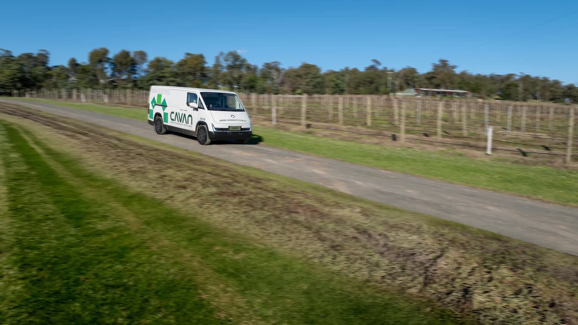 A Cavan electric van on an open gravel road beside a vineyard under a clear sky